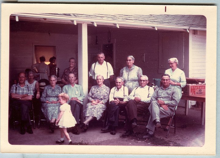 0673b.jpg - Christian Gerig Family 1965c  left to right:  Ben & Silvia Gerig, Fannie Roth, Christian & Mrs Gerig, Lizzie & Dan Roth, Martin & Emma Gerig, Amos Gerig, and Henry & Bertha Gerig.  Unknown girl in front and people in doorway.  Place known, but probably in Oregon somewhere.