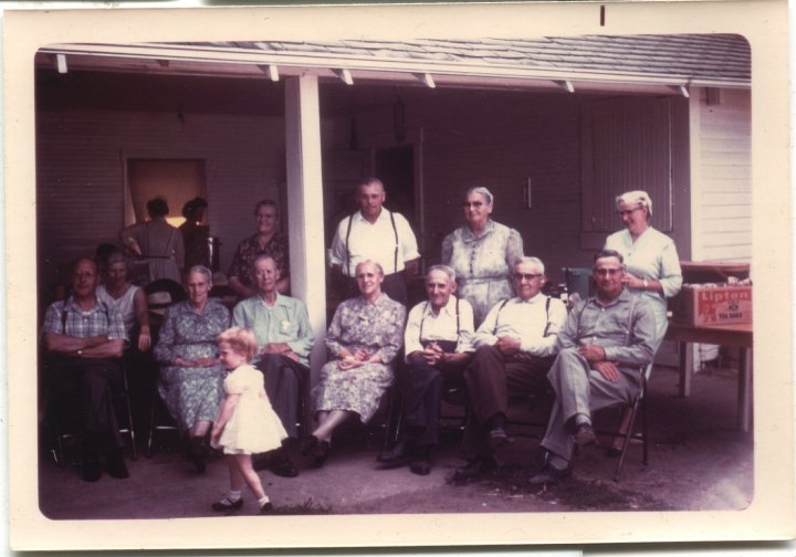 0673.jpg - Christian Gerig Family 1965c  left to right:  Ben & Silvia Gerig, Fannie Roth, Christian & Mrs Gerig, Lizzie & Dan Roth, Martin & Emma Gerig, Amos Gerig, and Henry & Bertha Gerig.  Unknown girl in front and people in doorway.  Place known, but probably in Oregon somewhere.